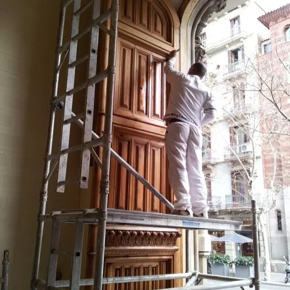 Barnizador de MCG restaurando un portal de madera modernista en Barcelona sobre andamio