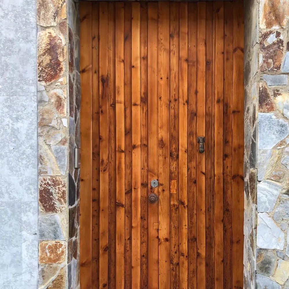 Puerta exterior de madera barnizada en fachada de piedra